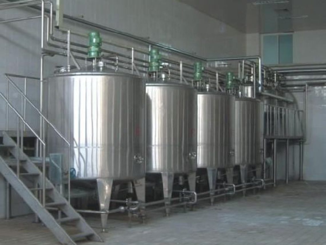 A row of stainless steel tanks sitting inside of a building.